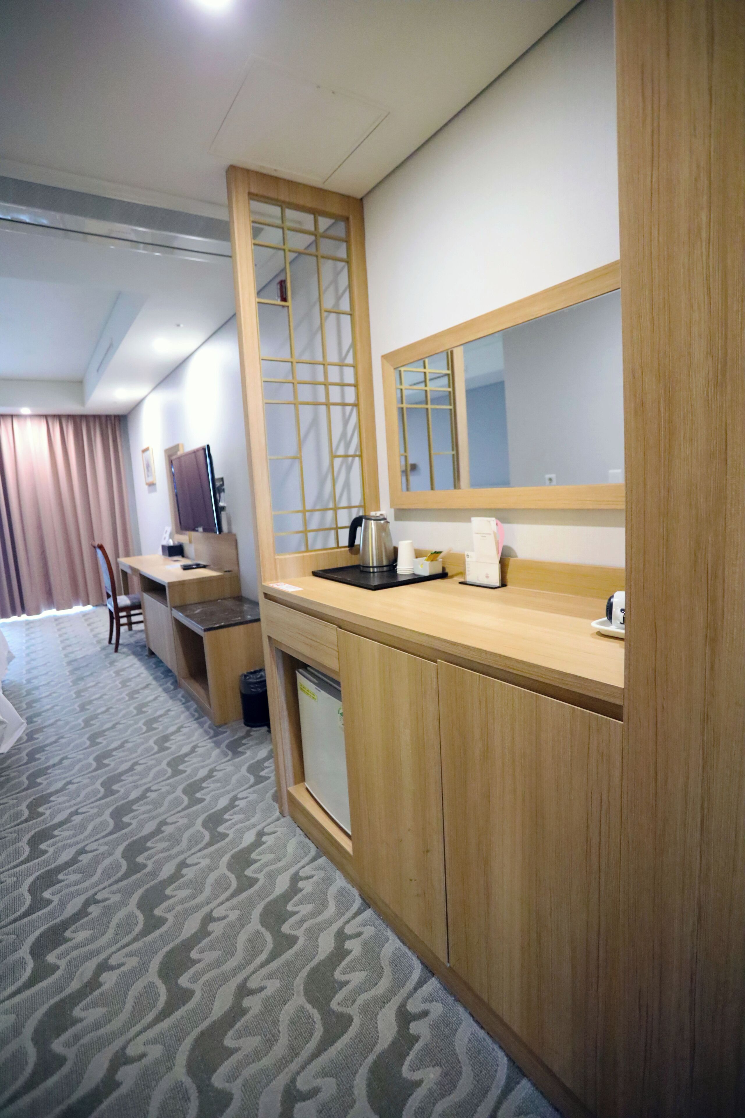 A hotel room with a wooden desk, a mirror, a coffee maker, and a small refrigerator.