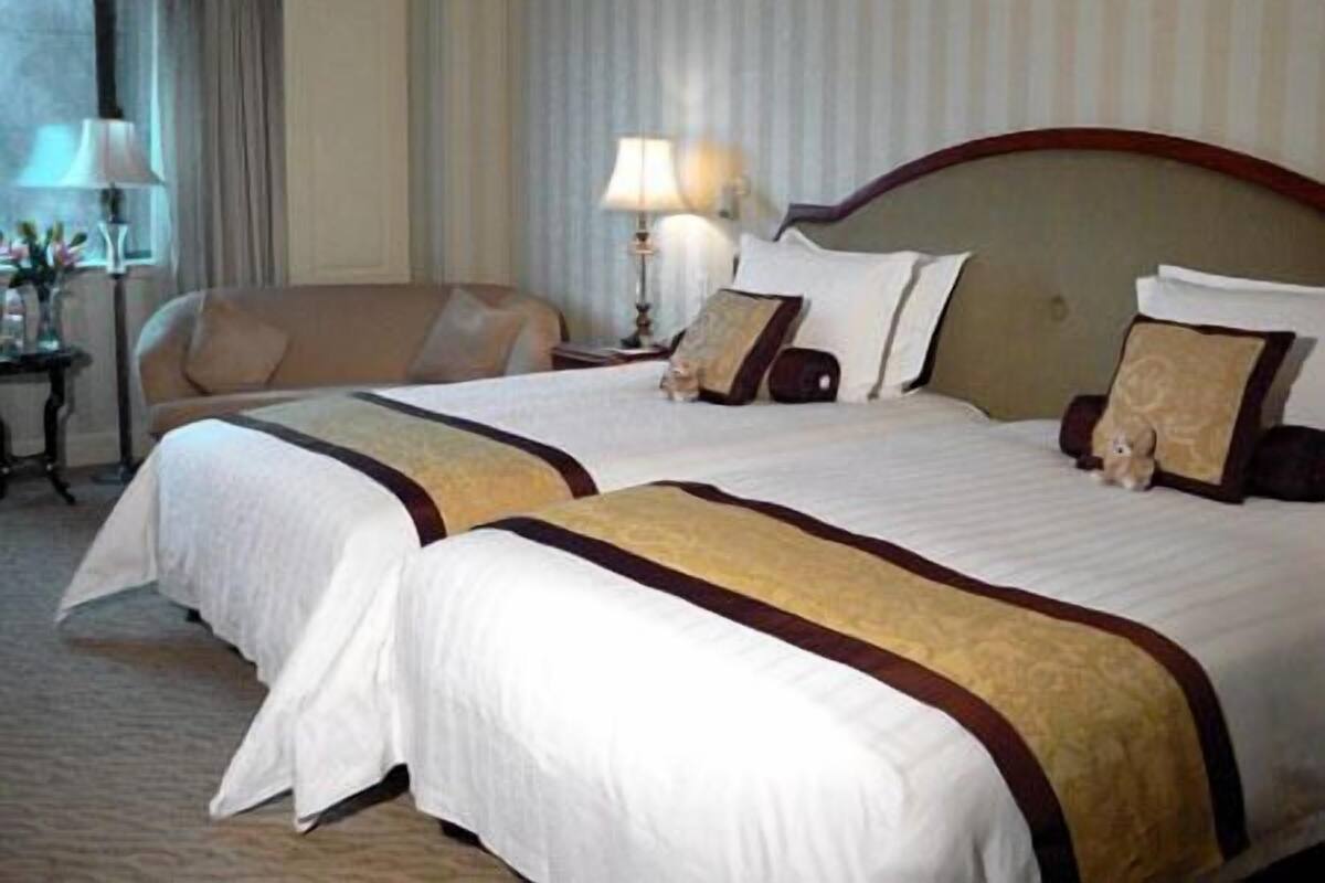 Een hotelkamer met twee bedden, een bank, een lamp en een raam met gordijnen.