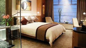 A hotel room with a large bed, a desk with a lamp, a view of the water, and a vase with flowers. - HARRIWAY GARDEN HOTEL CHANG AN (Dongguan)
