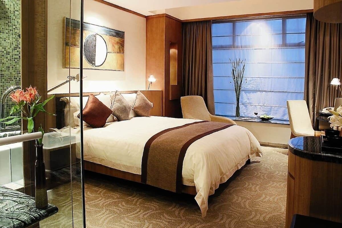 Een hotelkamer met een groot bed, een bureau met lamp, uitzicht op het water en een vaas met bloemen.