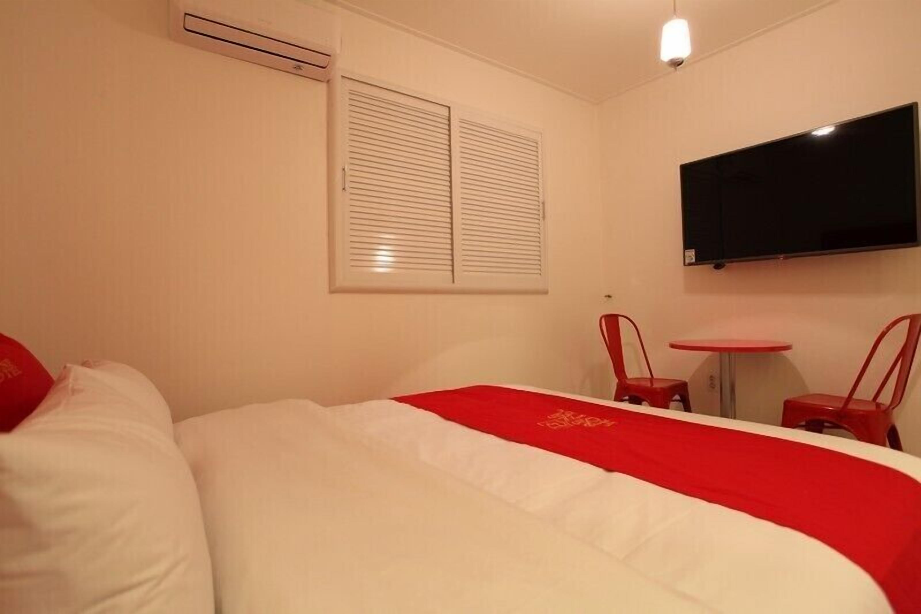 Una habitación de hotel con una cama, un televisor montado en la pared y una pequeña mesa con dos sillas.