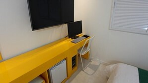 A compact room with a yellow desk, a black monitor, a keyboard, and a white chair.