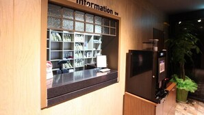 A reception desk with a computer, a refrigerator, and a plant.