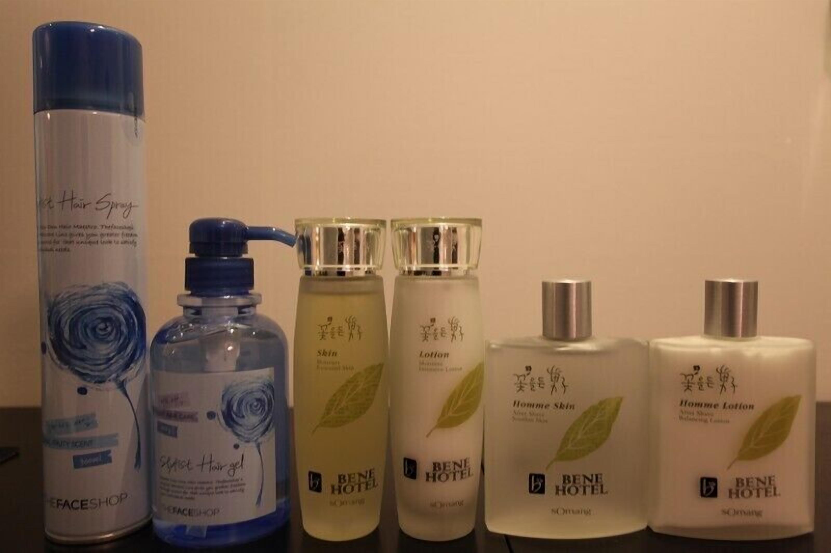 A row of hotel toiletries including a hair spray, a bottle of hair gel, and two sets of men's skin and lotion products.