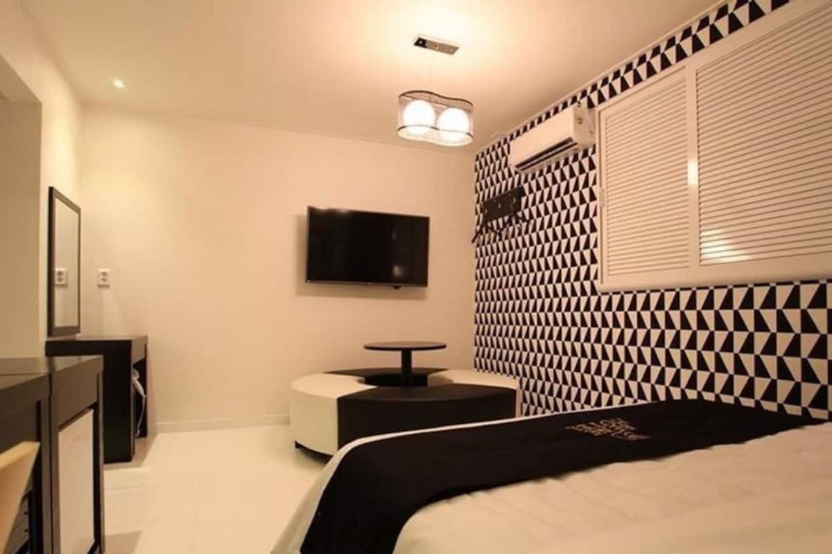 A bedroom with a bed, a flat-screen TV, a small table, and a patterned wall.