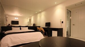 A modern hotel room with a large bed, a desk, a chair, a TV, and a door.