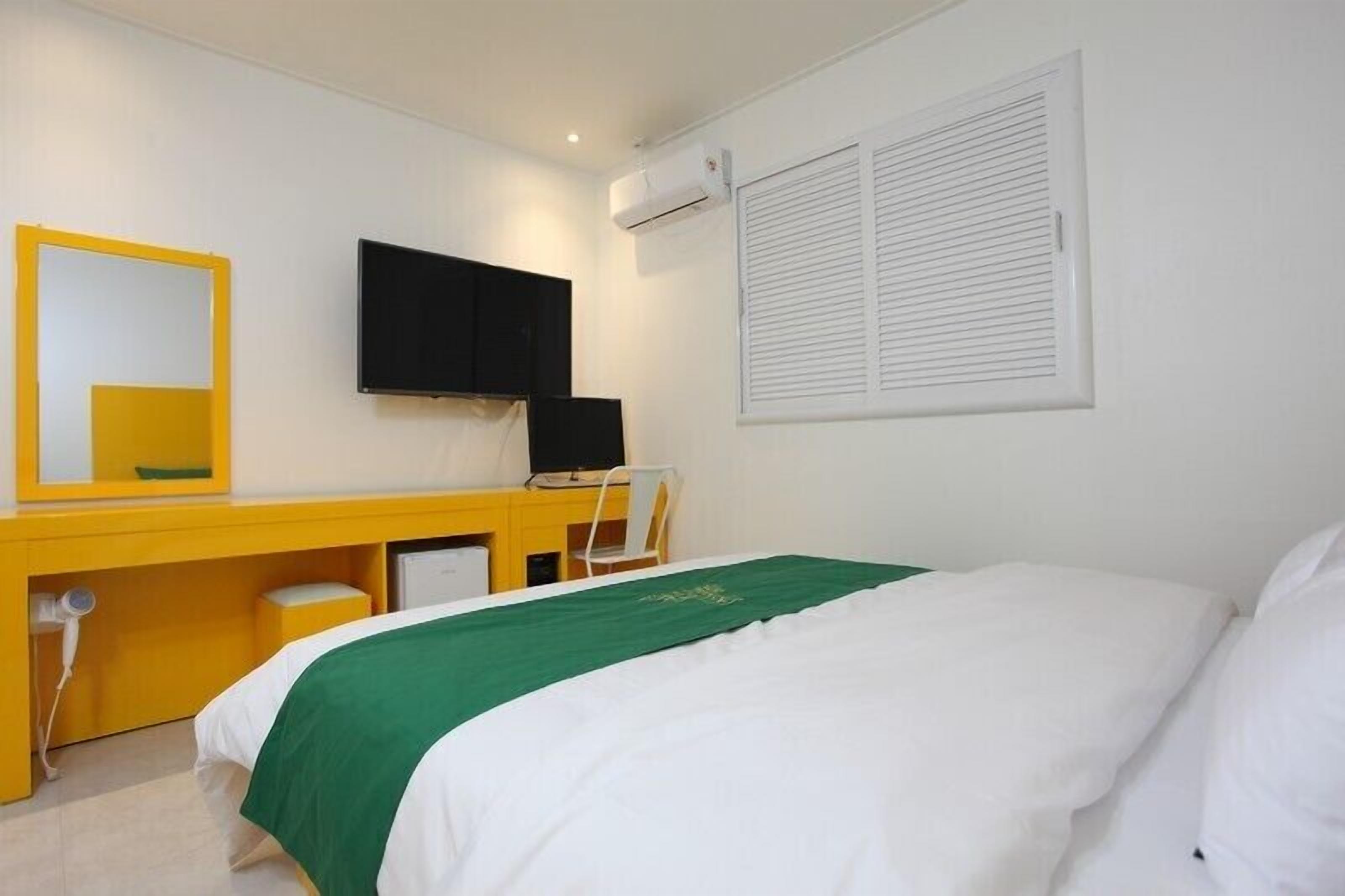 Una habitación de hotel con cama, escritorio con silla, televisión y aire acondicionado.
