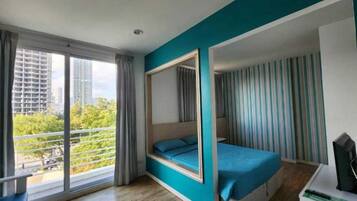 A modern hotel room with a large balcony, a bed, a desk, and a TV.