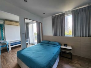 A bedroom with a bed, a desk, a chair, a window with curtains, and a door leading to a balcony.