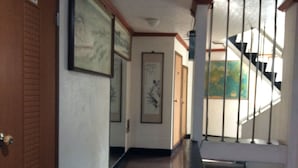 A hallway with framed artwork on the walls, a wooden door on the left, and a staircase with metal railings leading to an upper floor. - Busan Jang Motel (Busan)
