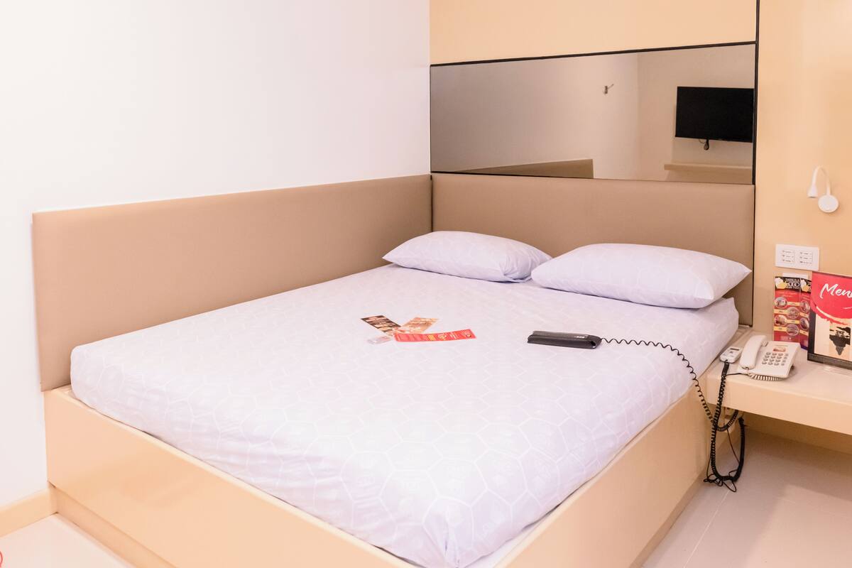 A neatly made bed with a white sheet and two pillows, a bedside phone, and a magazine on the bed.