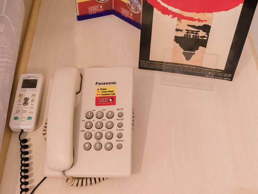 Een Panasonic telefoon op een houten bureau, samen met een hotel brochure en een klein doosje.
