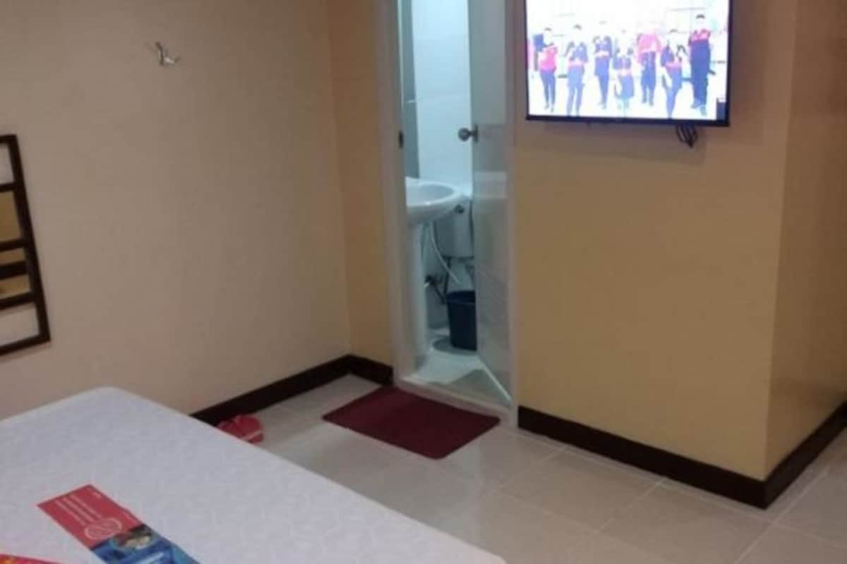 Habitación de hotel con cama, televisor montado en la pared y baño visible a través de una puerta abierta.