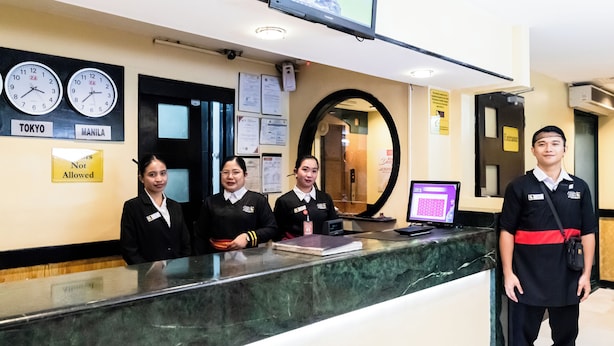 A reception desk with clocks displaying Tokyo and Manila times, a 'Not Allowed' sign, and a digital screen. - Hotel Sogo Novaliches (Quezon City)