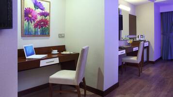 A hotel room with a desk, laptop, chair, and a painting of flowers on the wall.