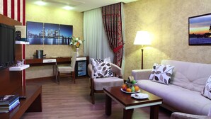 Habitación de hotel con sofá, sillón, mesa de comedor y televisor.