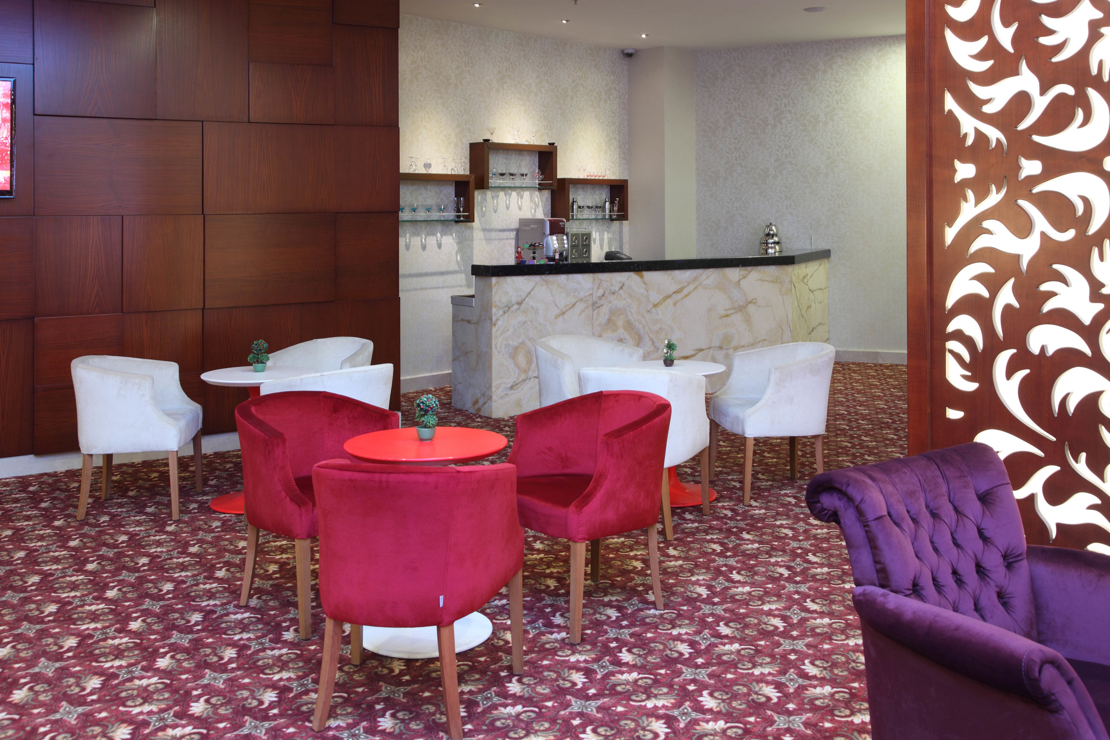Een hotel lobby met een marmeren receptiebalie, witte en rode stoelen en een kamerbreed tapijt met dessin.