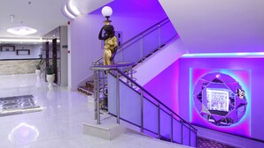 Un vestíbulo moderno con piso de mármol, una escalera con barandales de metal y una estatua decorativa.