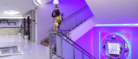 A modern lobby with a marble floor, a staircase with metal railings, and a decorative statue.