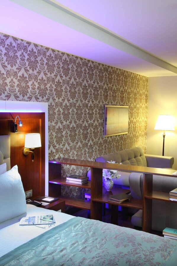 A hotel room with a bed, a desk, a chair, and a bookshelf.