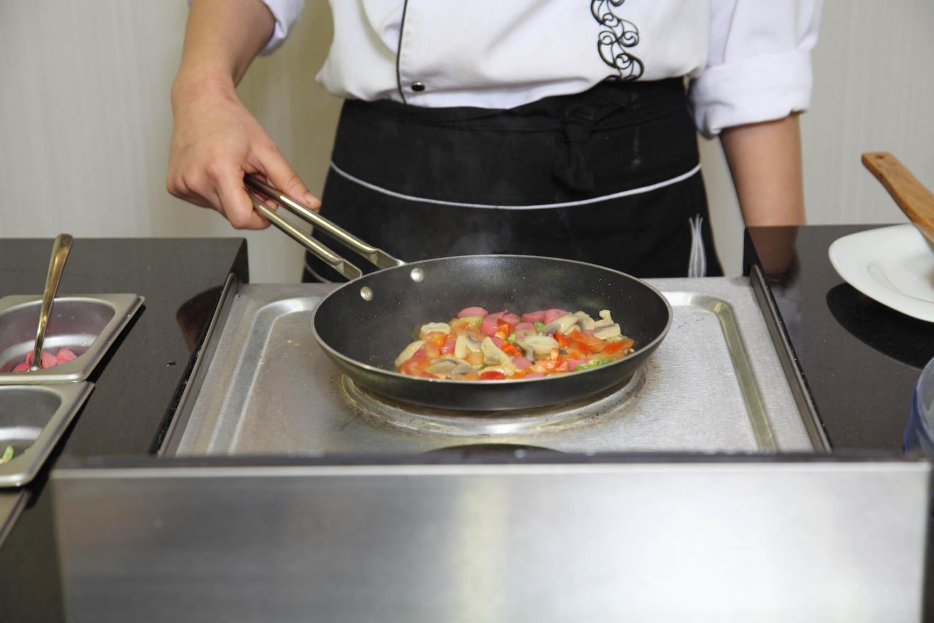 A person cooking in a kitchen with a pan on a stove.