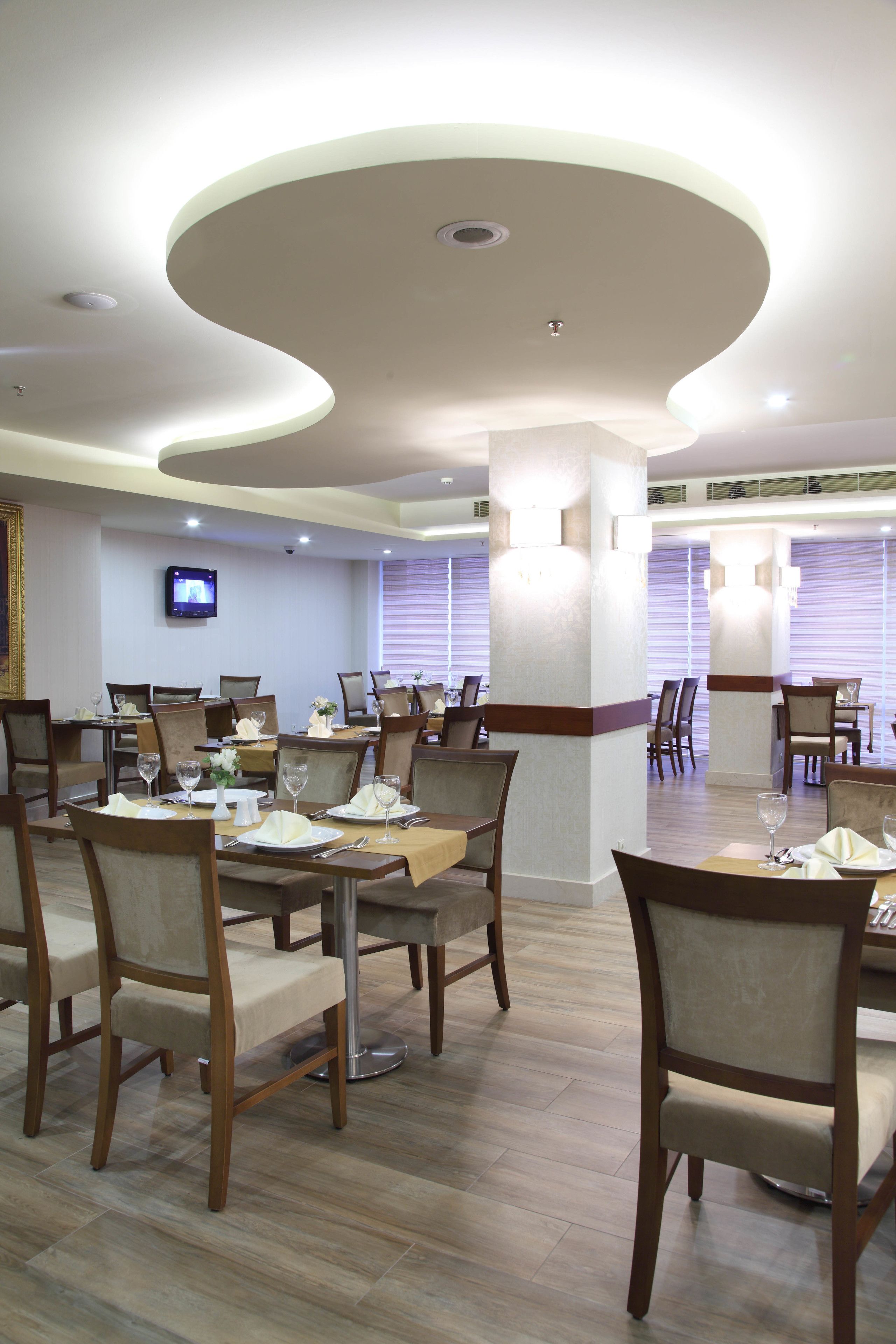 A dining area with tables set for service, wooden chairs, and a television mounted on the wall.