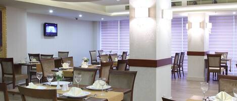 A dining area with tables set for service, wooden chairs, and a television mounted on the wall.