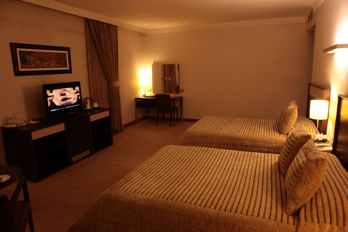 A hotel room with two beds, a desk, a television, and a lamp.