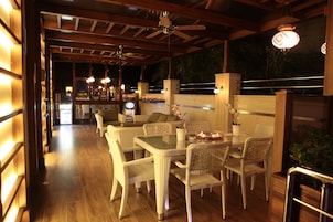 Un área de comedor al aire libre con mobiliario de mimbre, piso de madera y ventiladores de techo.
