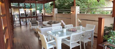 An outdoor patio with wicker furniture, a glass-top table, and hanging lanterns.