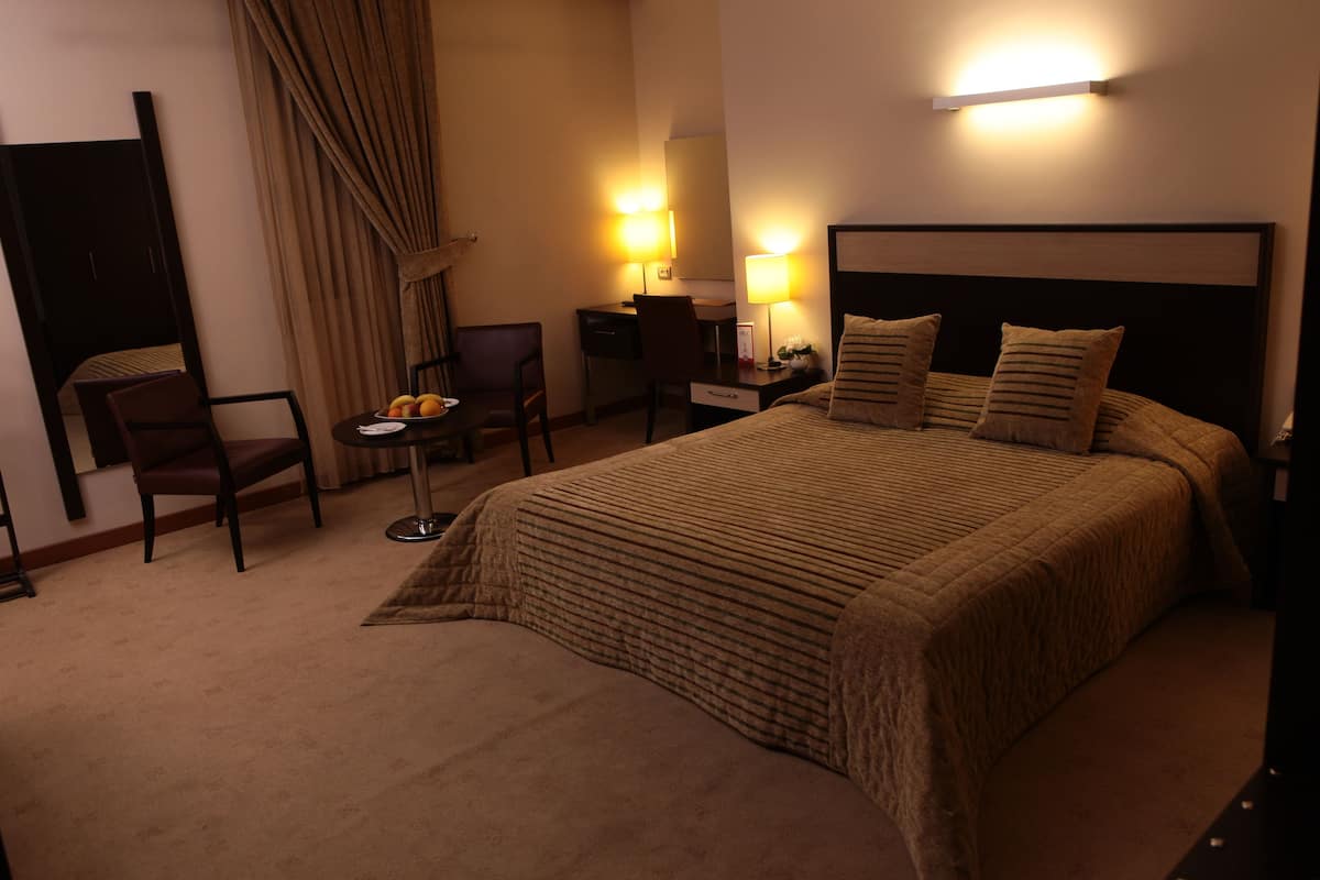 A hotel room with a large bed, a desk, a chair, and a small table with a fruit bowl.