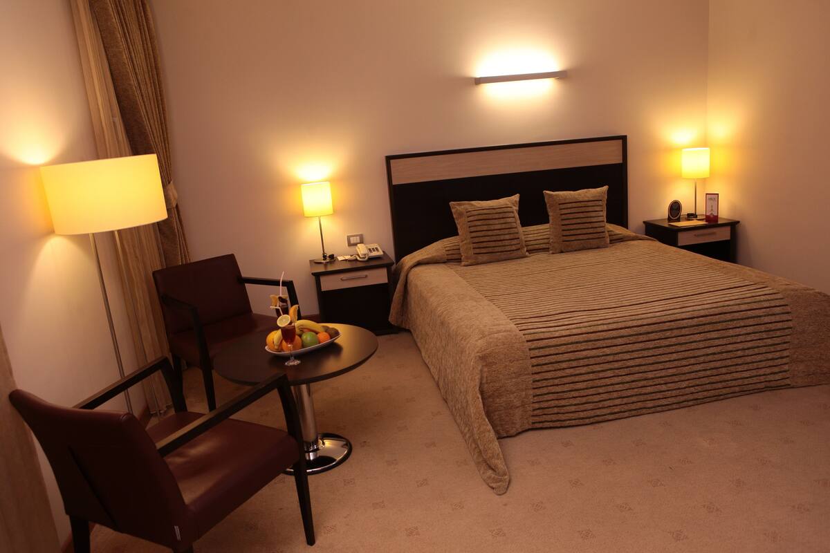 A hotel room with a bed, bedside tables, a desk with a chair, and a lamp.