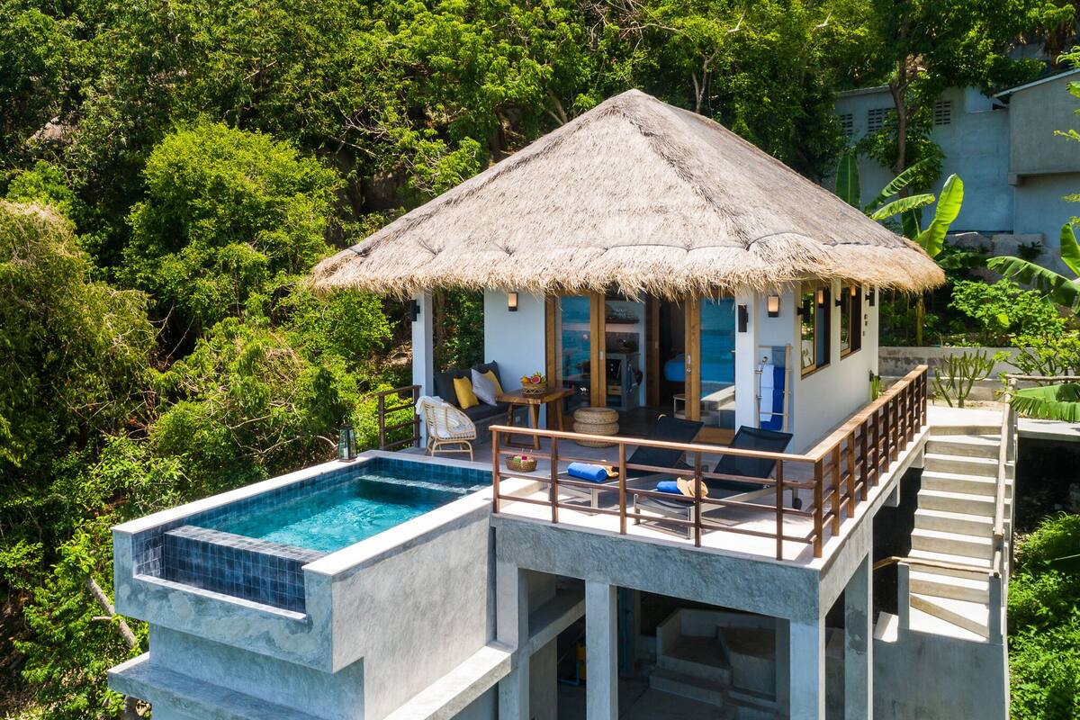 A thatched-roof bungalow with a pool and a deck.