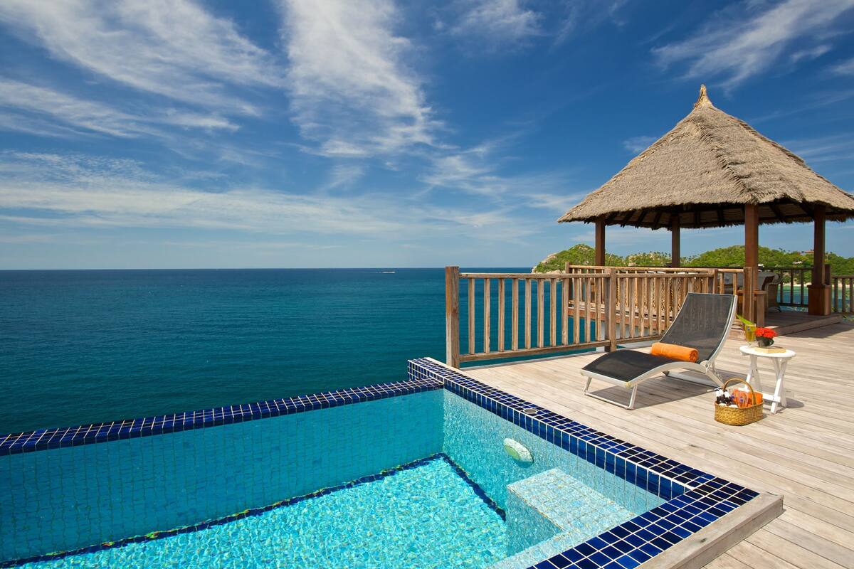A poolside area with a thatched-roof gazebo, lounge chairs, and a view of the ocean.