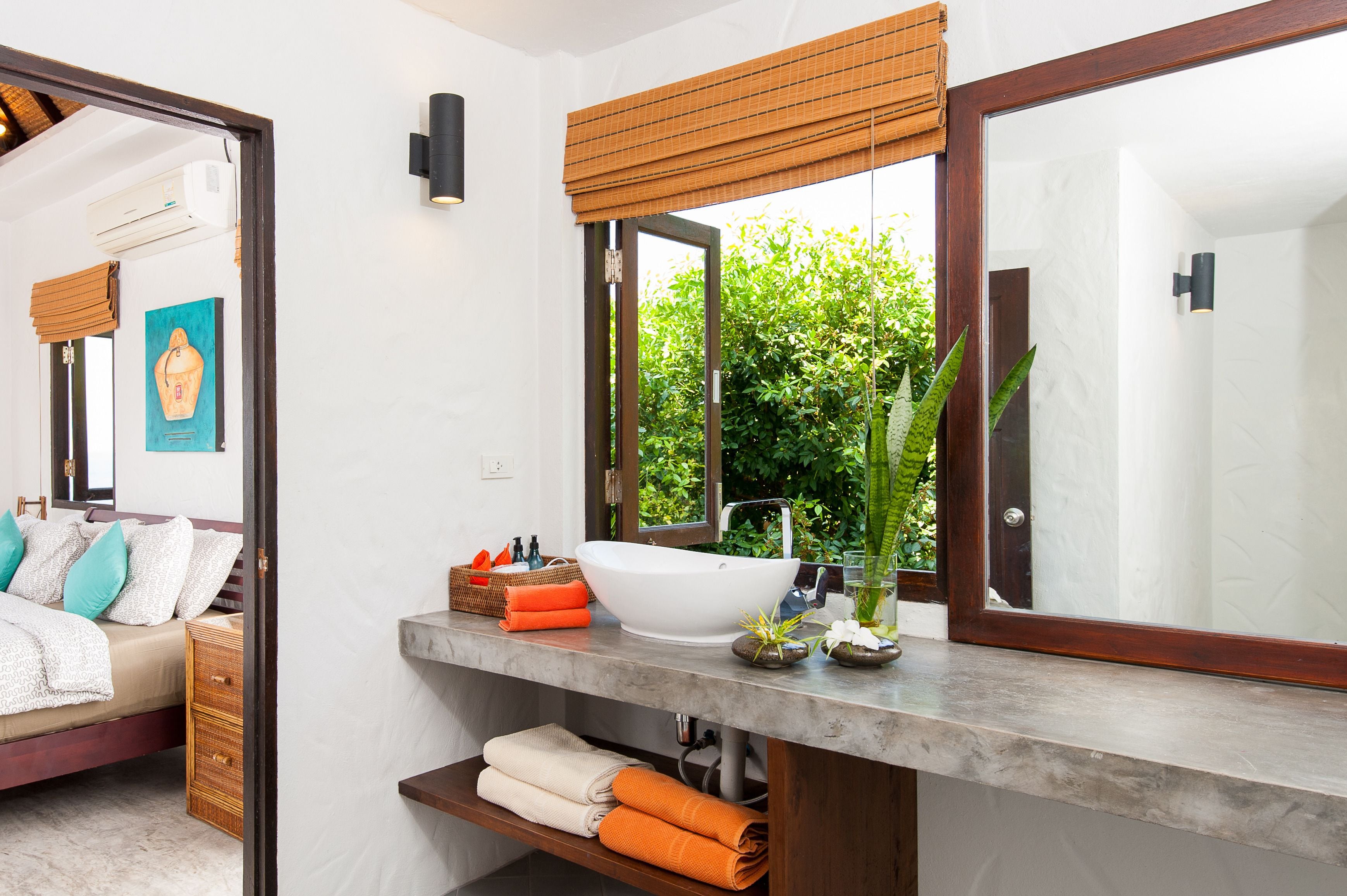 A bathroom with a large mirror, a white sink, and a window with a view of greenery.