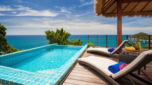 A swimming pool with a view of the ocean, lounge chairs, and a thatched roof structure.