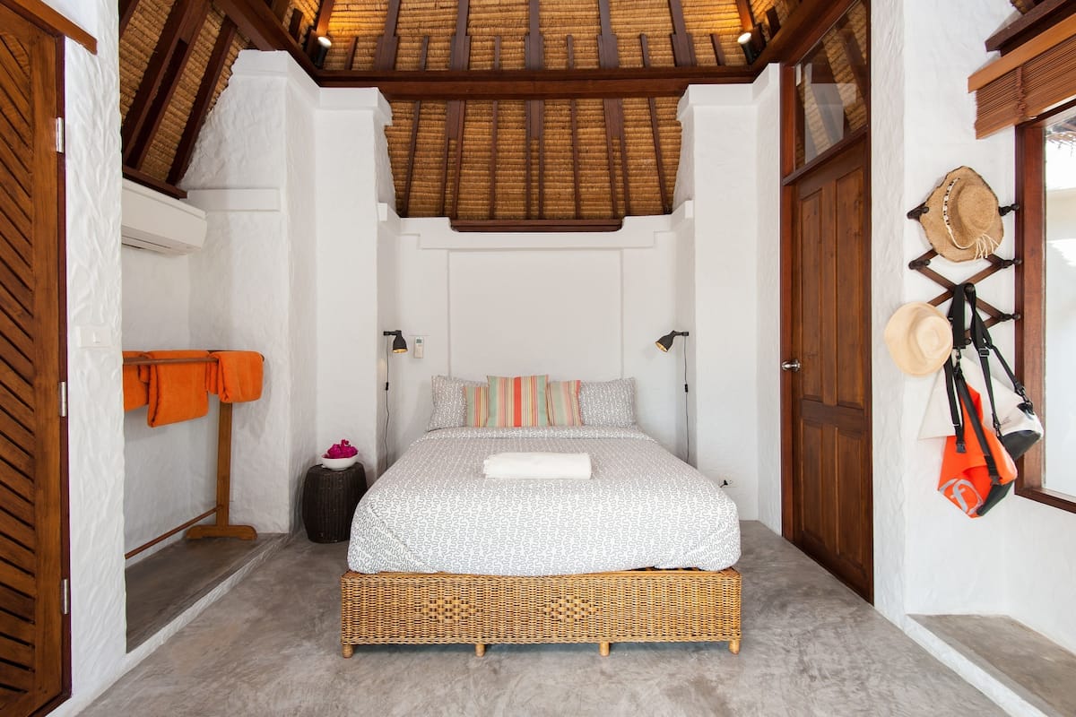 A bedroom with a bed, a nightstand, a wall-mounted hat rack, and a wooden ceiling.