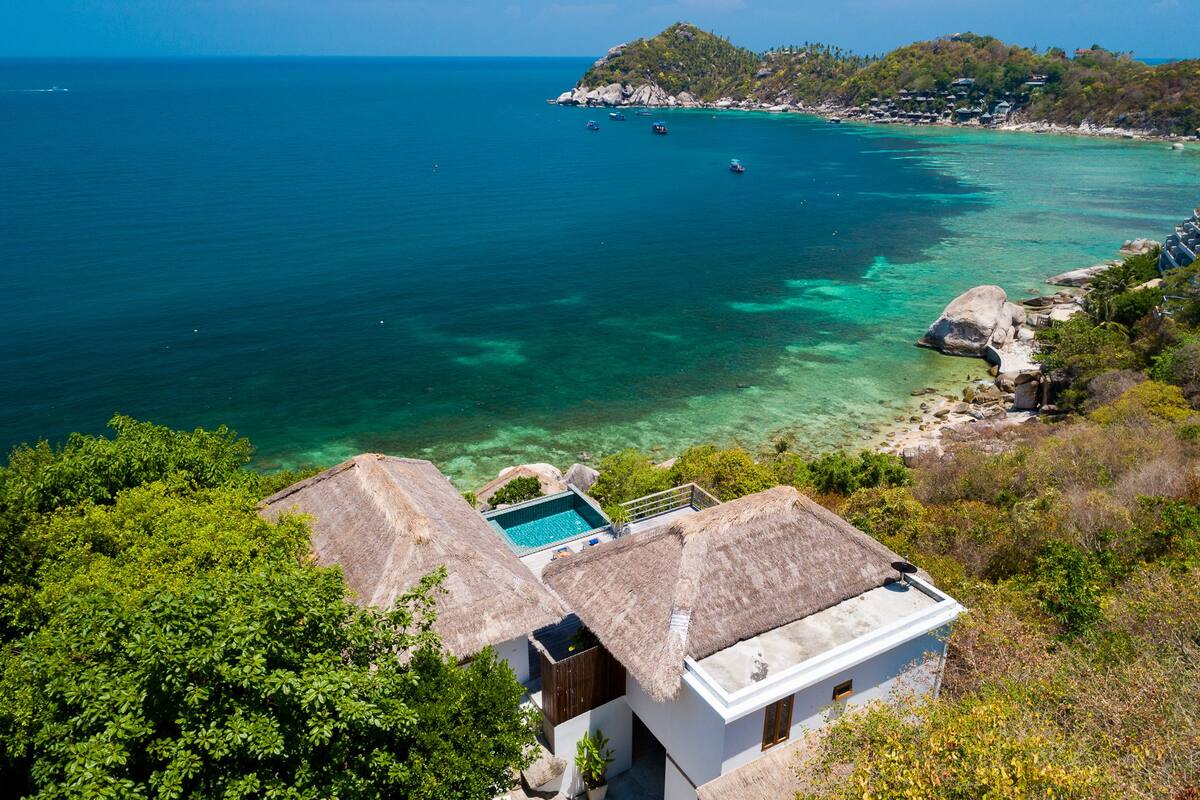 A coastal property with a pool, thatched-roof buildings, and a view of the sea.