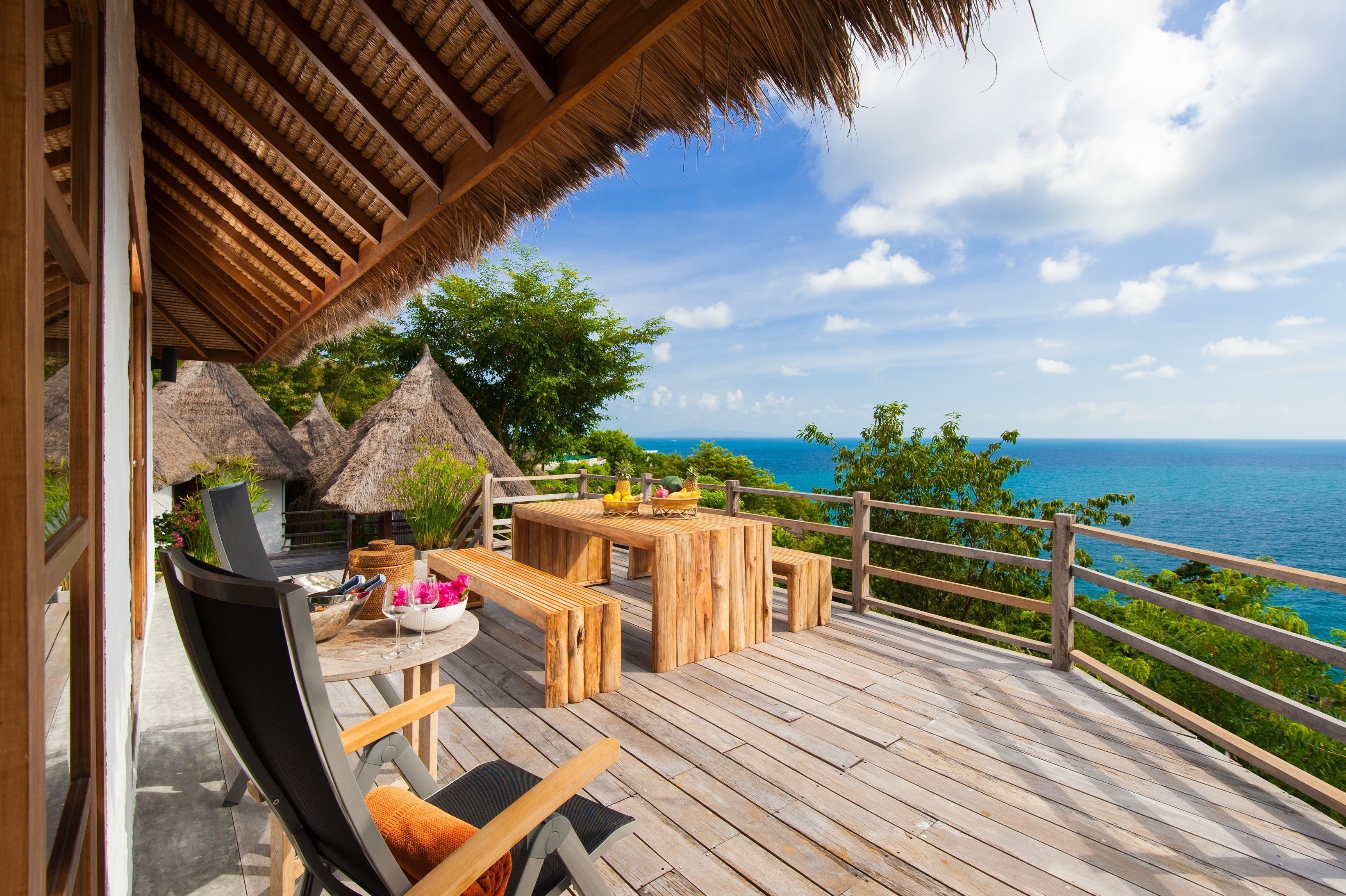 A wooden deck with a table and chairs, overlooking a scenic ocean view.