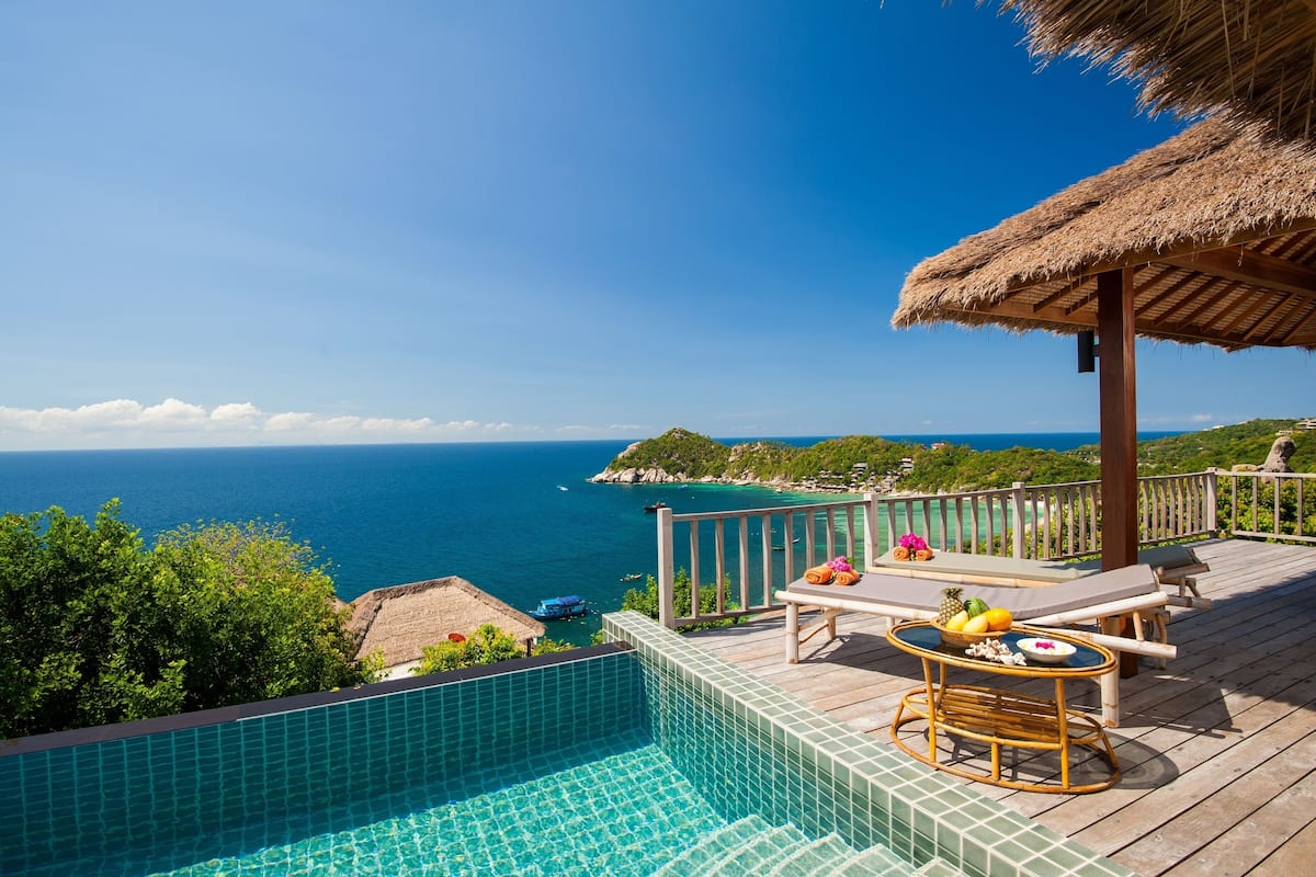 A poolside area with a view of the ocean, a thatched roof, and lounge chairs.