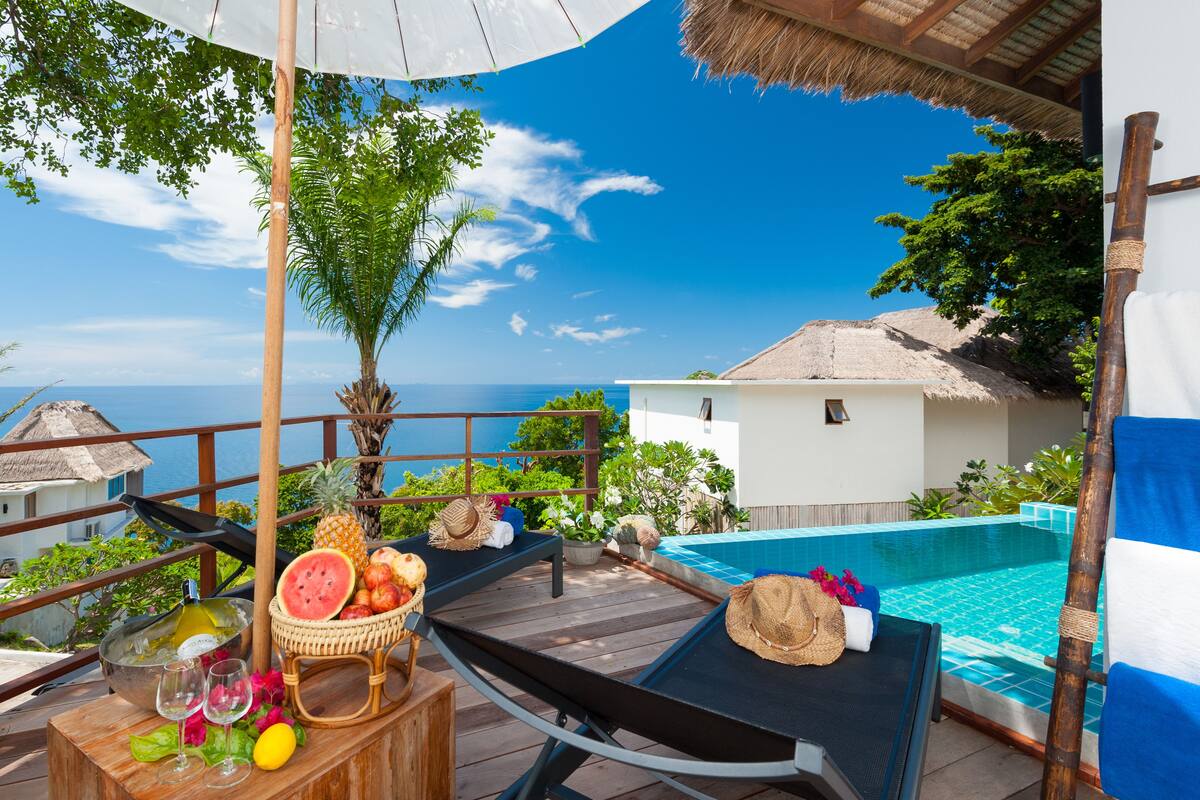A wooden deck with a pool, tropical plants, and a view of the ocean.