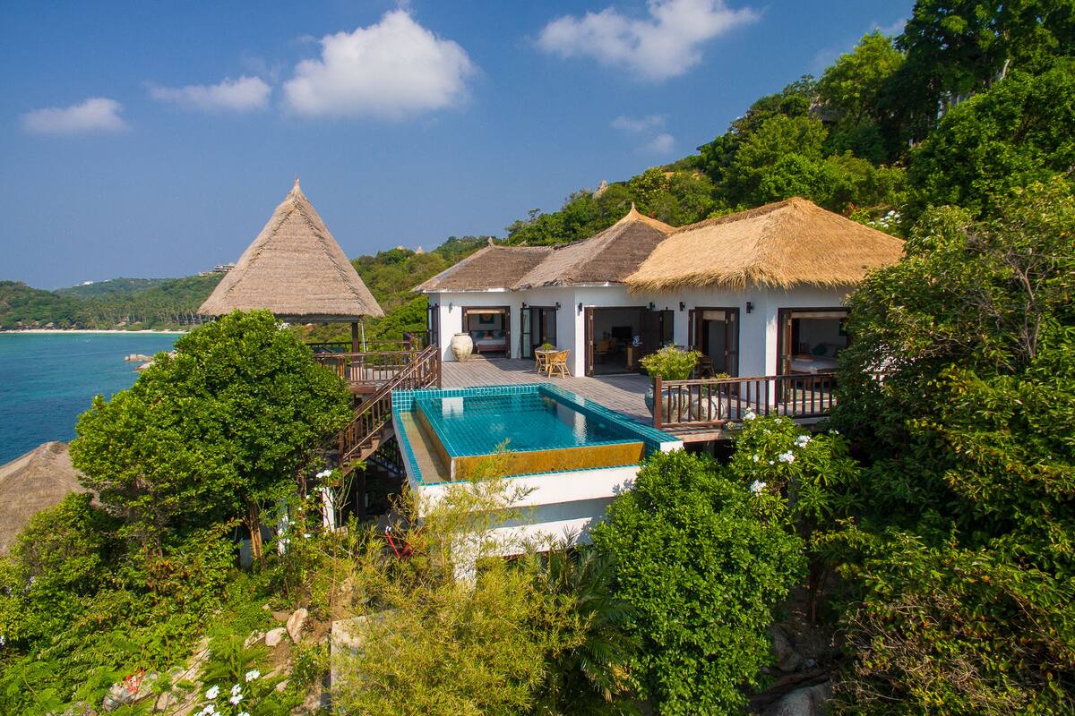 A resort with a pool, thatched-roof buildings, and lush greenery.
