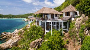 A coastal house with a thatched roof, a balcony, and a view of the sea.