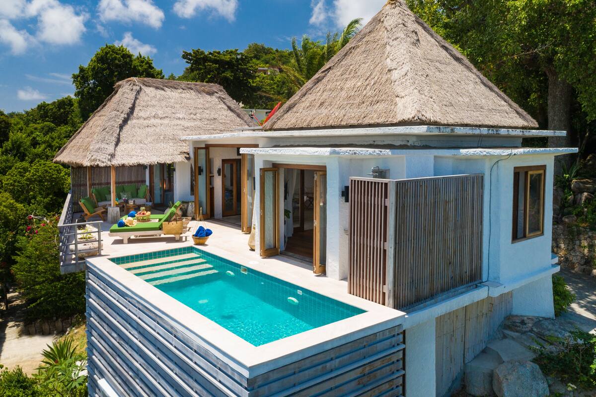 A resort with a swimming pool, thatched-roof structures, and lush greenery.
