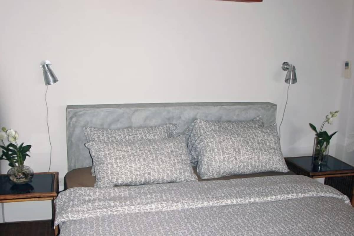 A bedroom with a bed, two bedside tables, two lamps, and two potted plants.