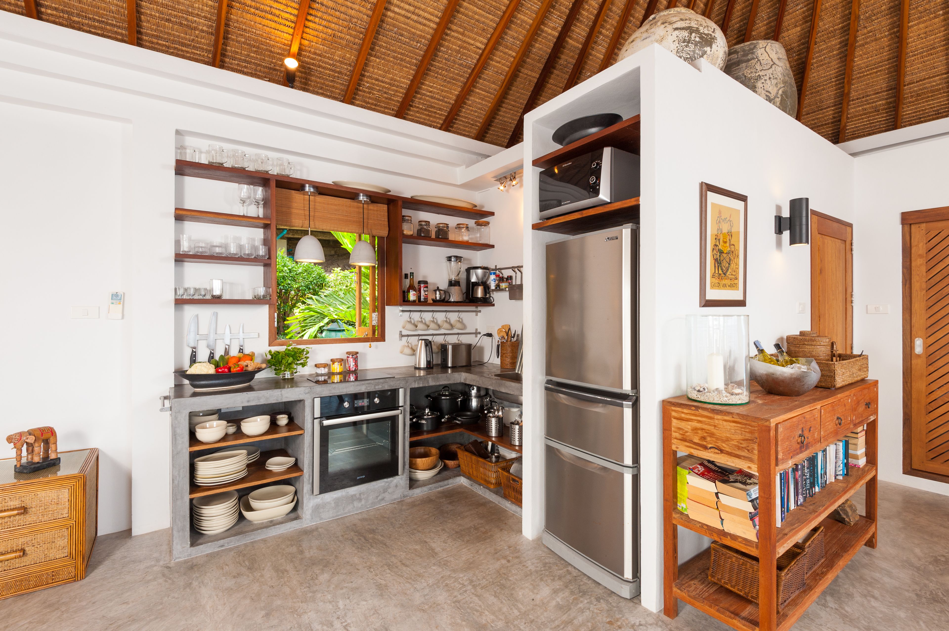 Una cocina moderna con un refrigerador empotrado, estantes de madera y un área de comedor con una mesa y sillas.