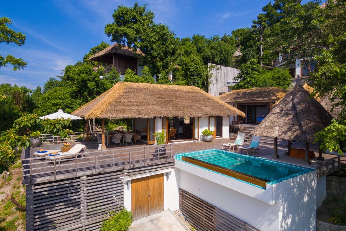 A pool area with a thatched-roof structure, lounge chairs, and a wooden deck.