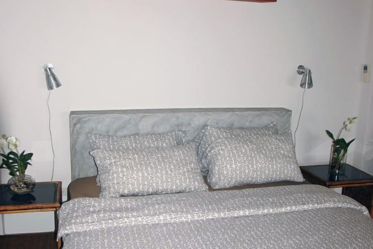 A bedroom with a bed, two bedside tables, two lamps, and two potted plants.