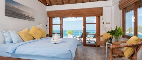 A bedroom with a bed, a view of the ocean, a ceiling fan, and a window with a view of the beach.