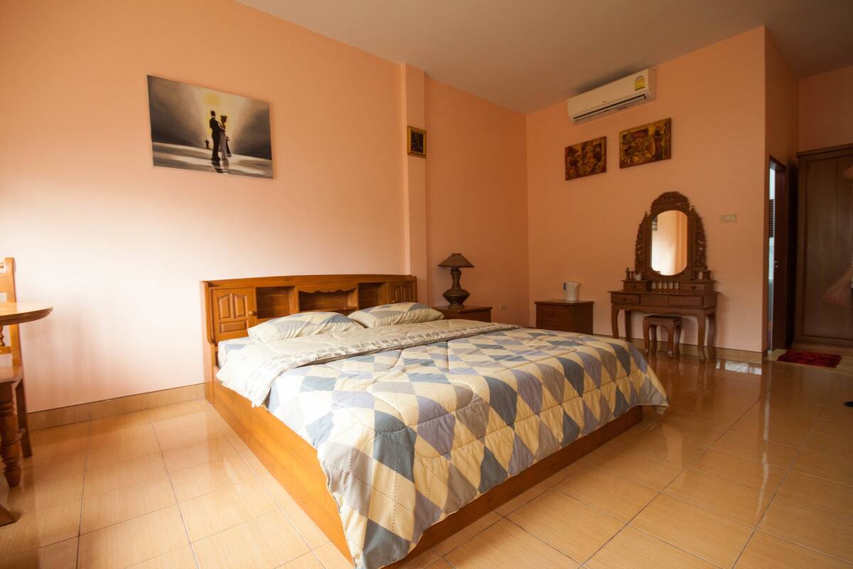 A bedroom with a wooden bed, a desk, a chair, a lamp, a mirror, and a painting on the wall.
